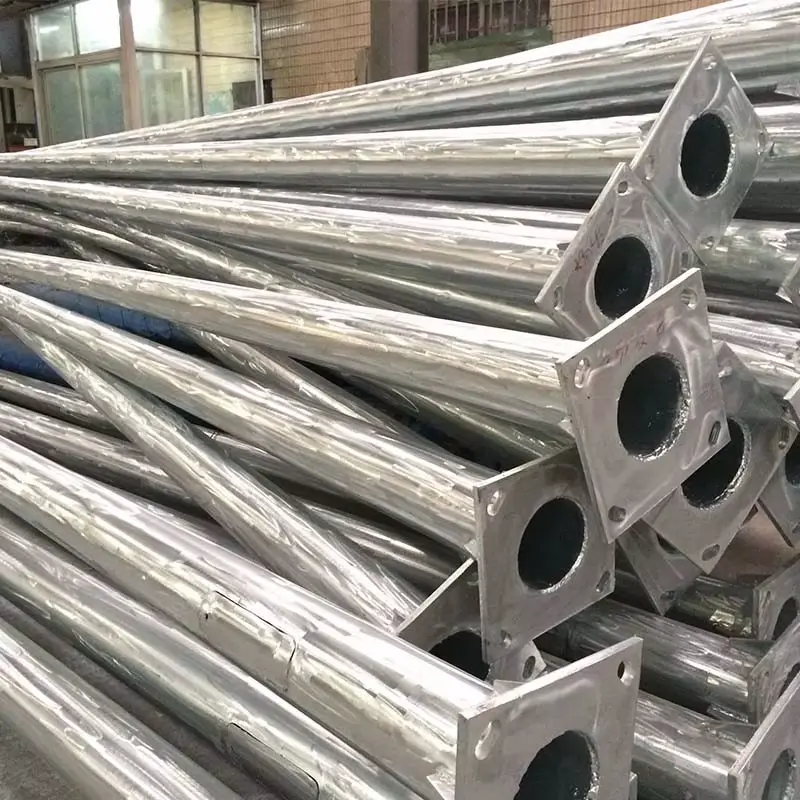 Pila de postes metálicos cónicos recién galvanizados por ORBE - Postes Metalicos, apilados en fábrica y mostrando sus placas base listas para ser despachadas.